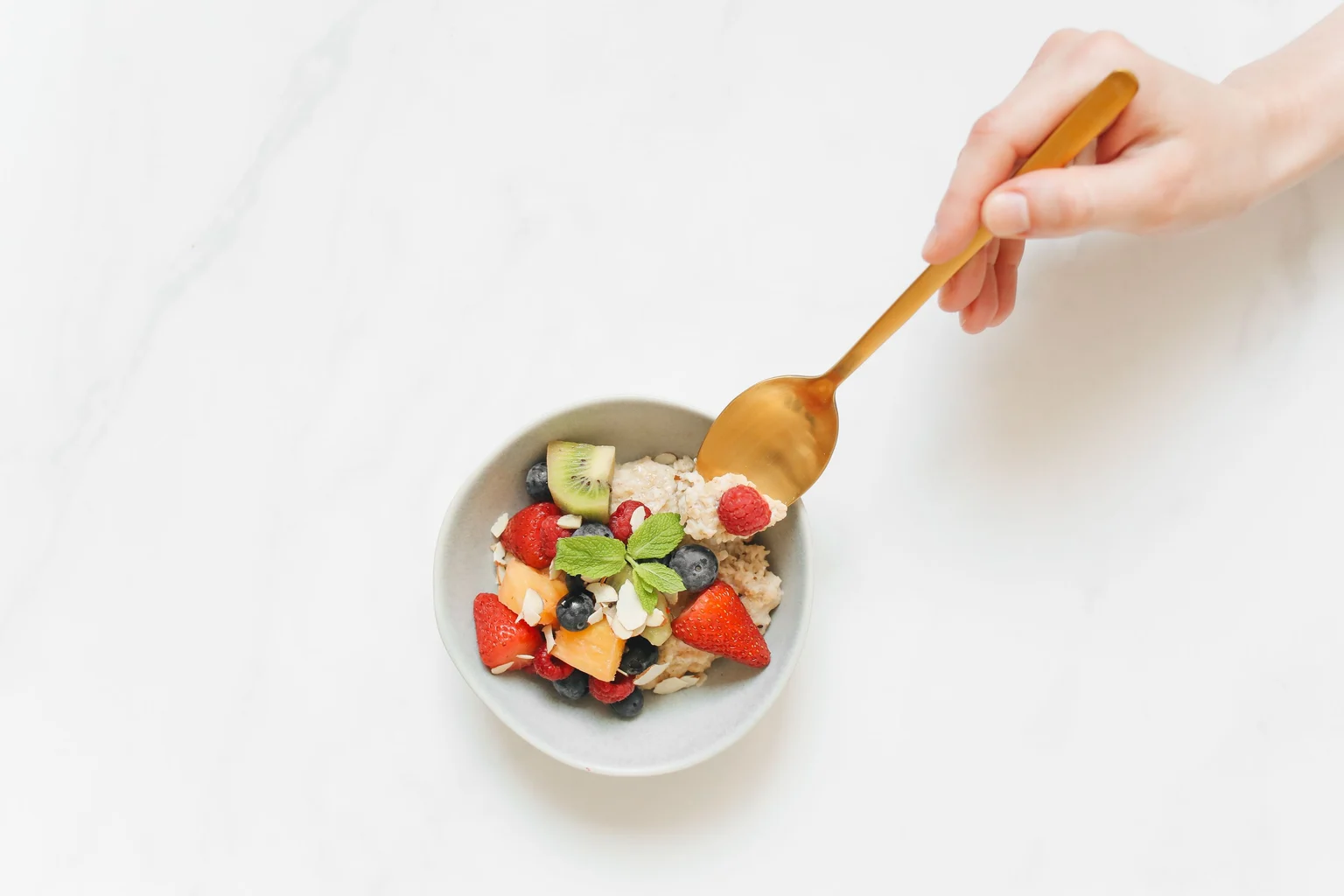 A spoon reaching into a bowl of oats and colourful fruit.