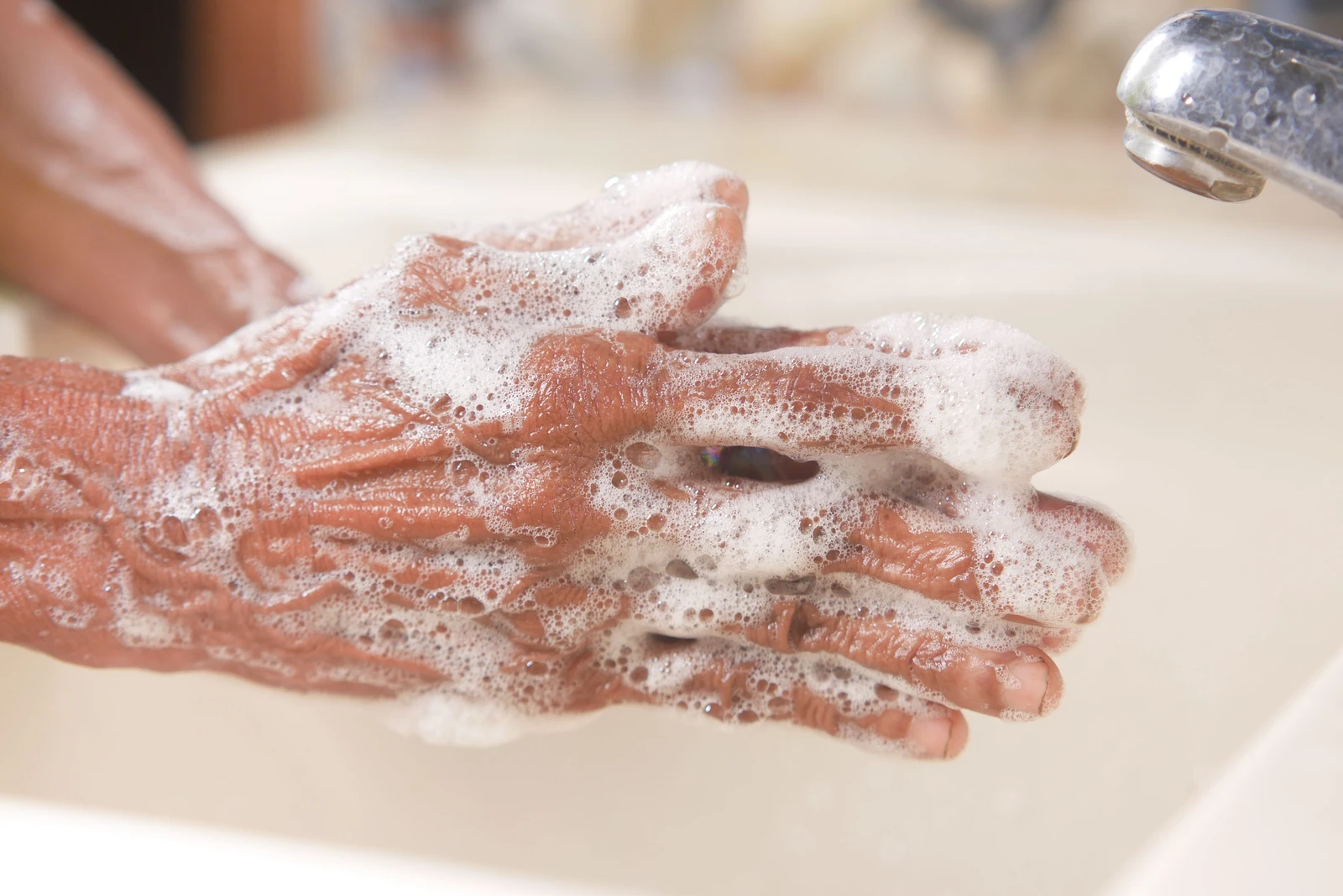 Hands covered in soap lather at a bathroom sink.