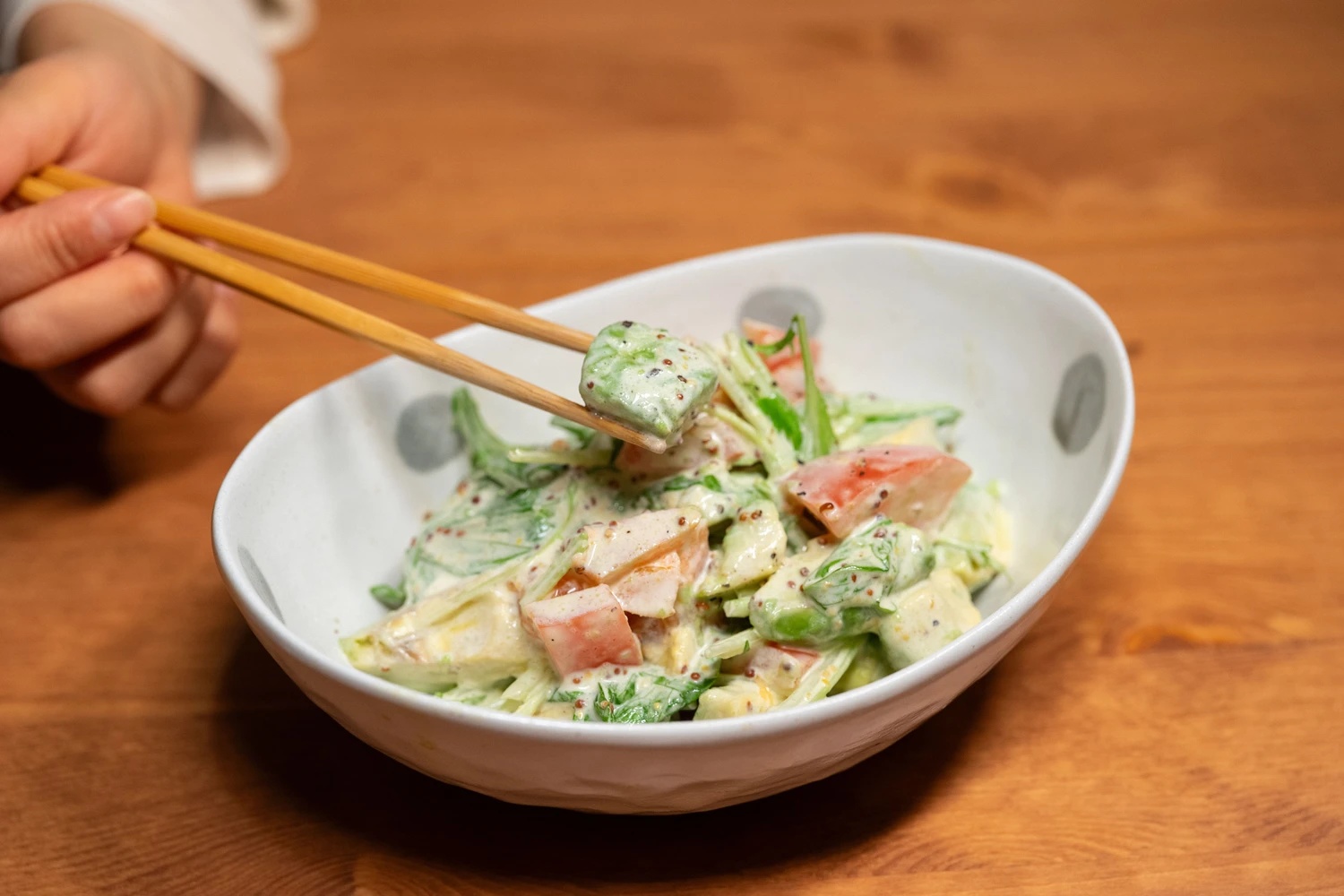 Chopsticks lift a dressed vegetable from a creamy salad.