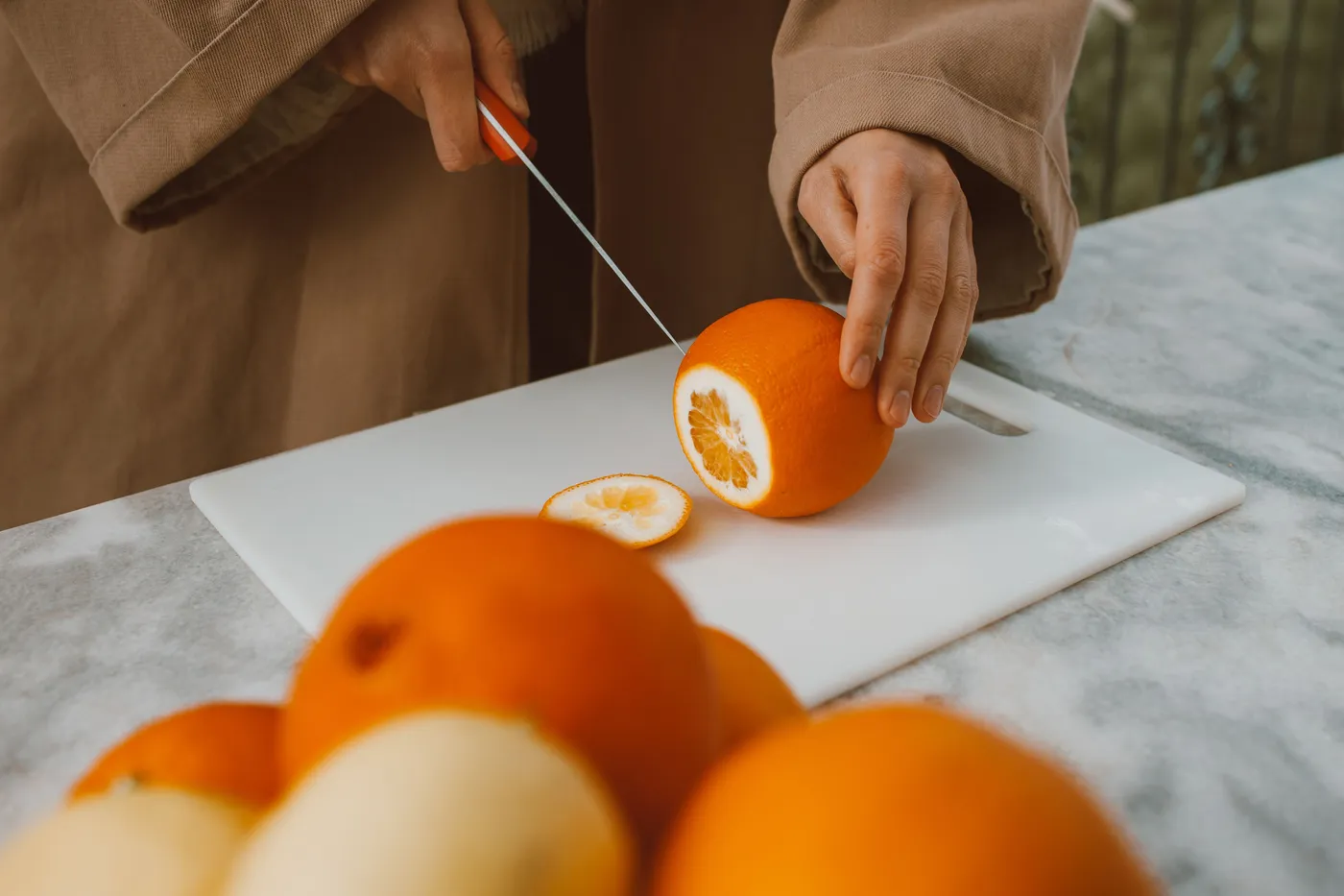 Hands slice a fresh orange on a clean cutting board.