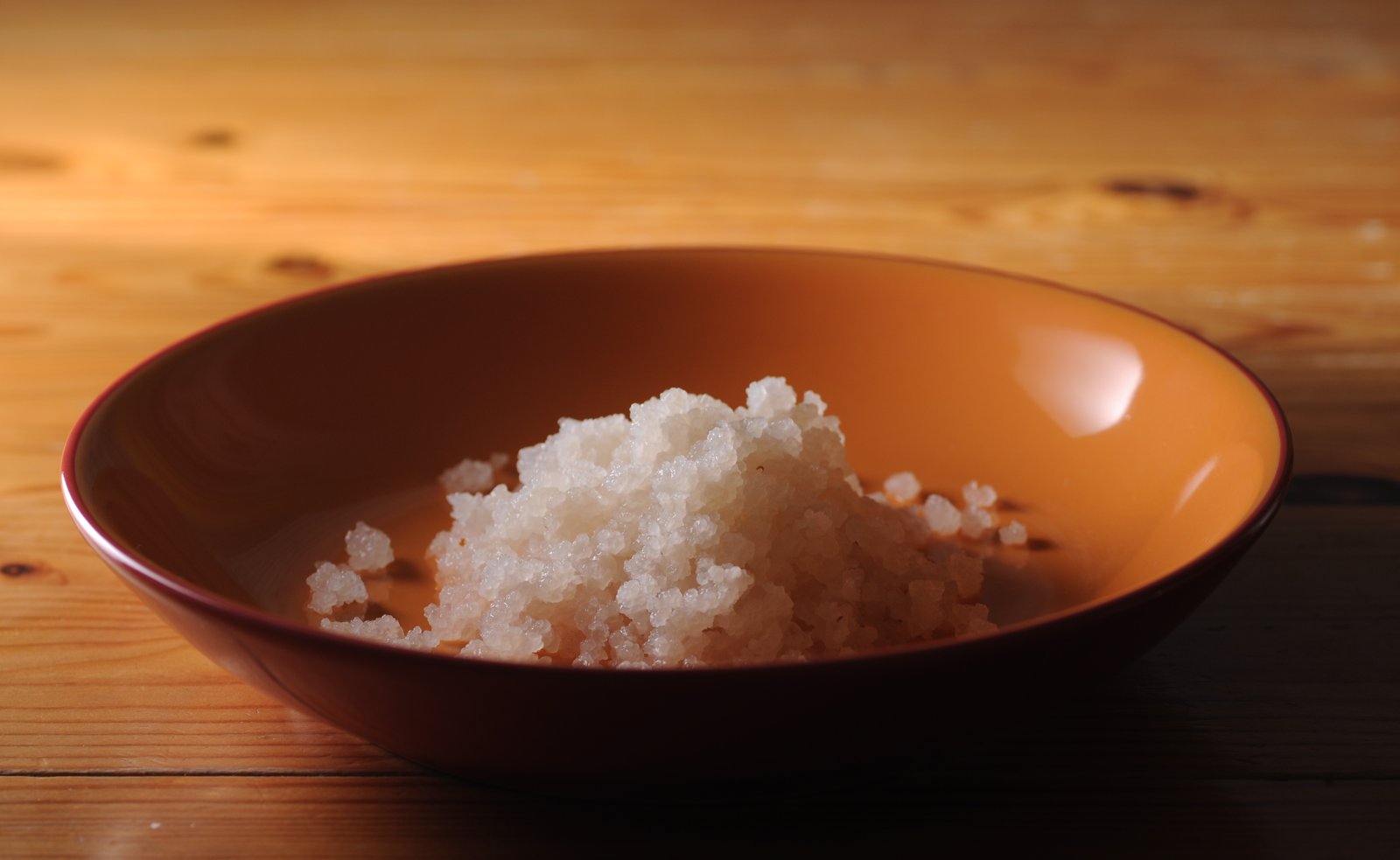 Translucent water-kefir grains in a brown ceramic bowl on a wooden table.